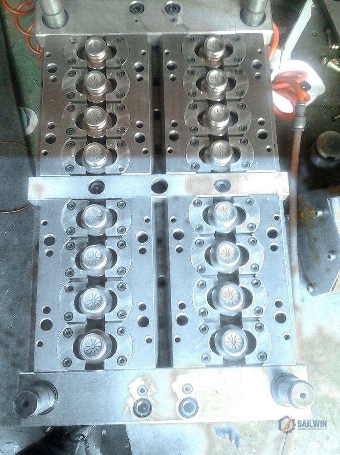 16-cavity water cap injection mold on workbench with distressed blue floor and cooling hoses Sailwin